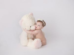 Sweet portrait of a small child sitting with a large white teddy bear against a neutral background.