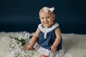 Baby in navy blue and white dress sitting on white fur rug.