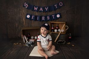 Baby photo with baseball theme and Way To First banner in dark wood setting.