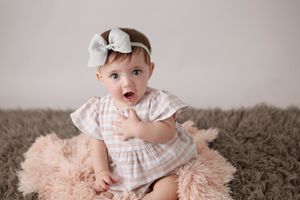 Baby in white dress on pink fur rug during photo session.