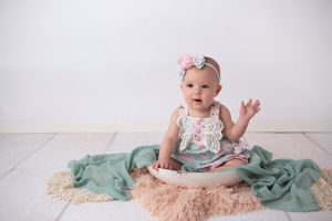 Baby in floral outfit sitting on teal and beige textured blankets.