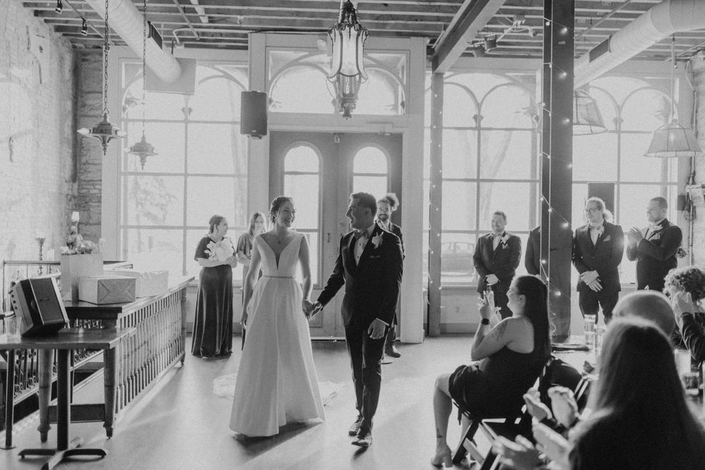 Newlyweds walk hand in hand down aisle after ceremony as guests applaud indoors.