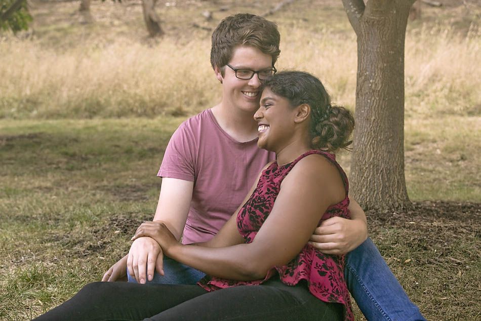 A couple sharing an intimate moment while sitting under a tree.