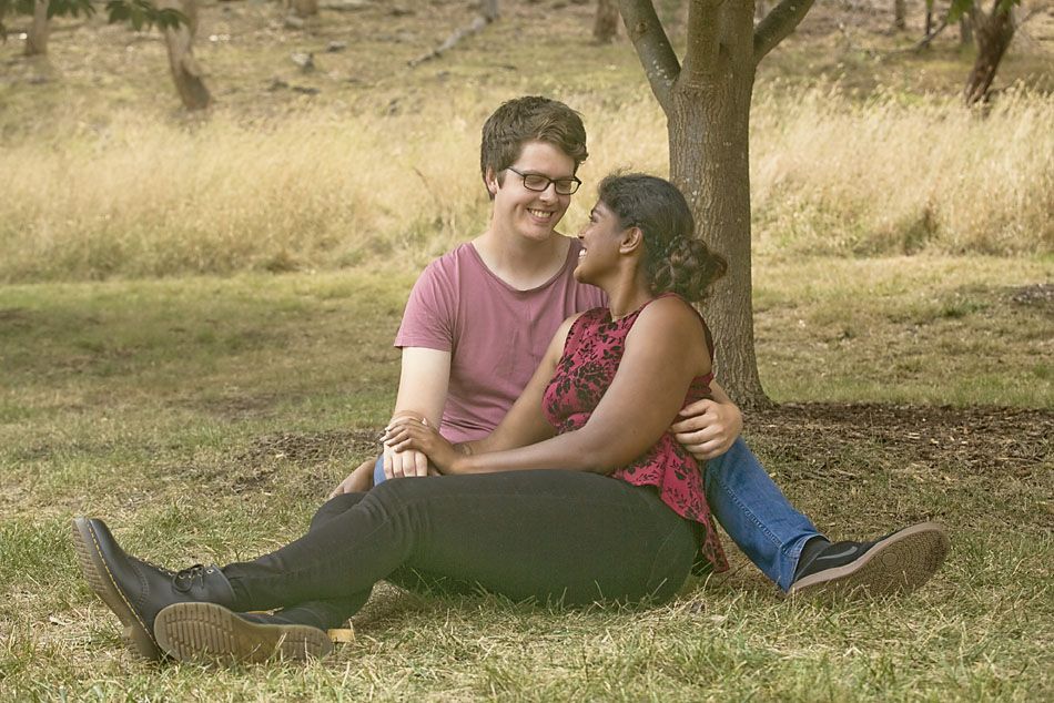 A couple sitting together on grass under a tree sharing a tender moment.
