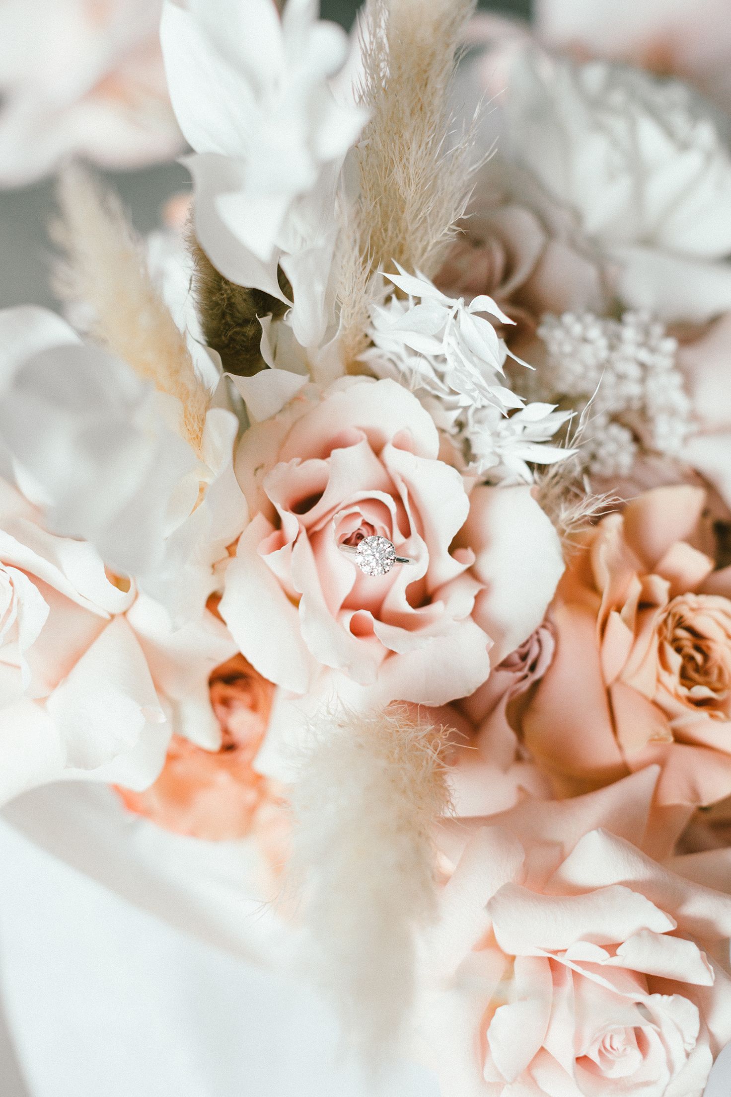 Romantic bouquet of blush pink roses with white feathers and dried elements in soft focus.