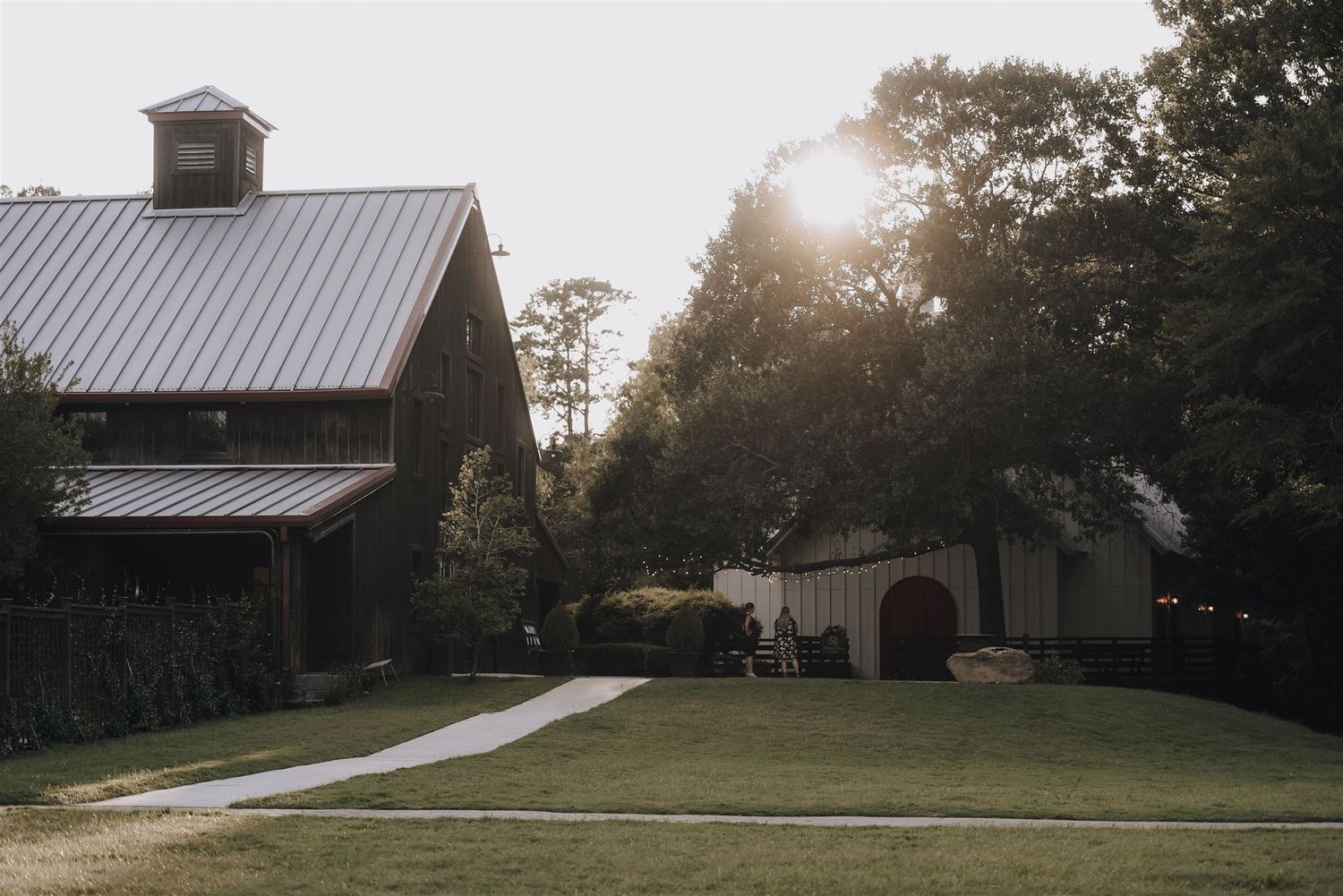 Rustic barn and outbuilding with metal roof at sunset on manicured lawn.