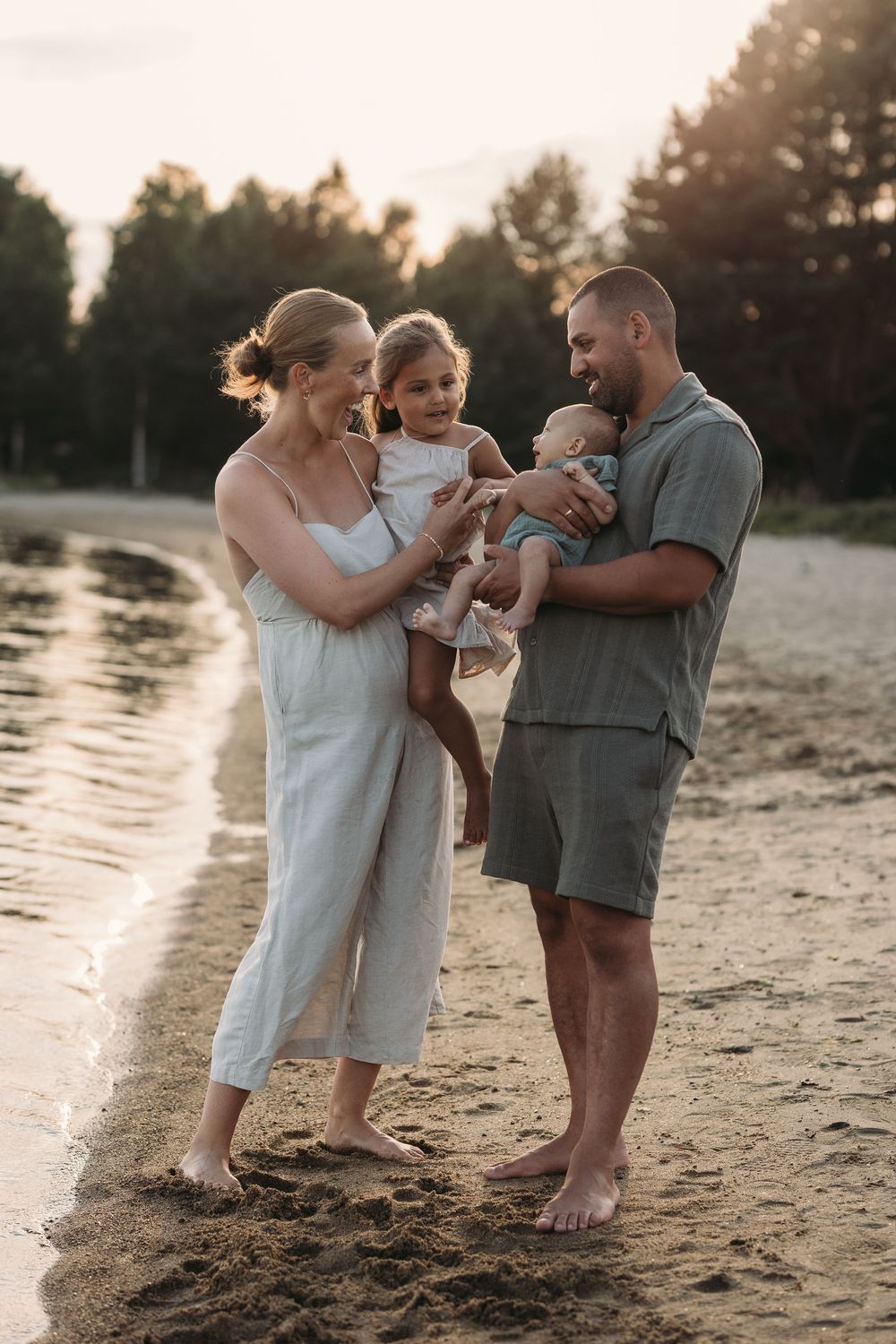 familie på fire med to små barn som står tett sammen på stranden i varmt lys fra solnedgangen