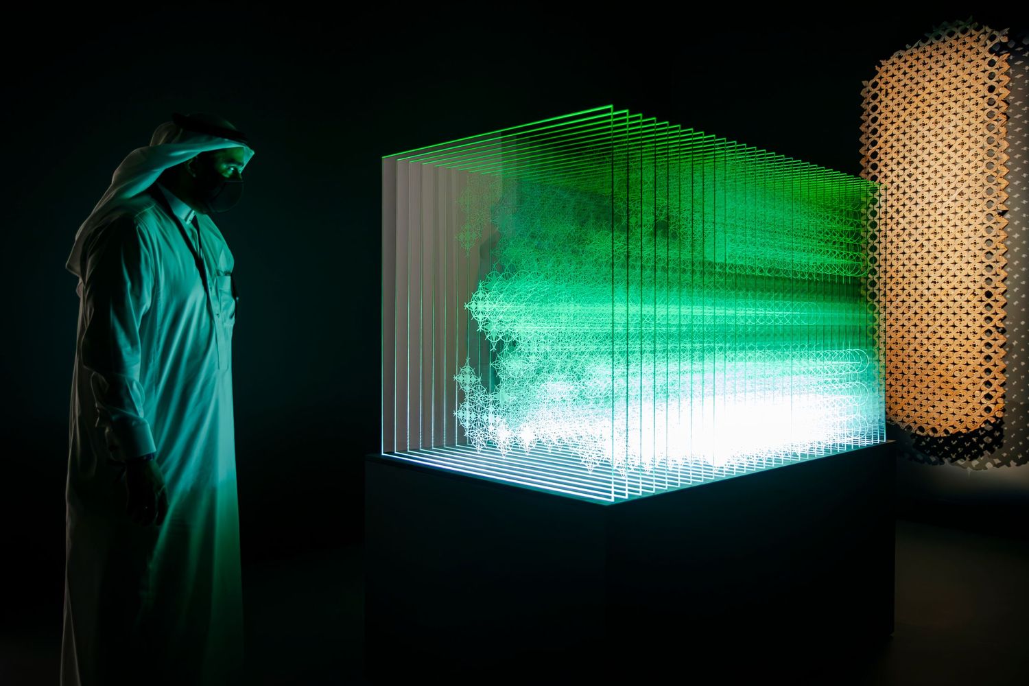 A glowing green light installation creates an ethereal cube-like structure in a dark exhibition space.