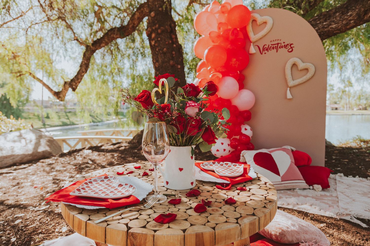 Romantic Valentine's Day picnic setup with red balloons and table decor under tree.