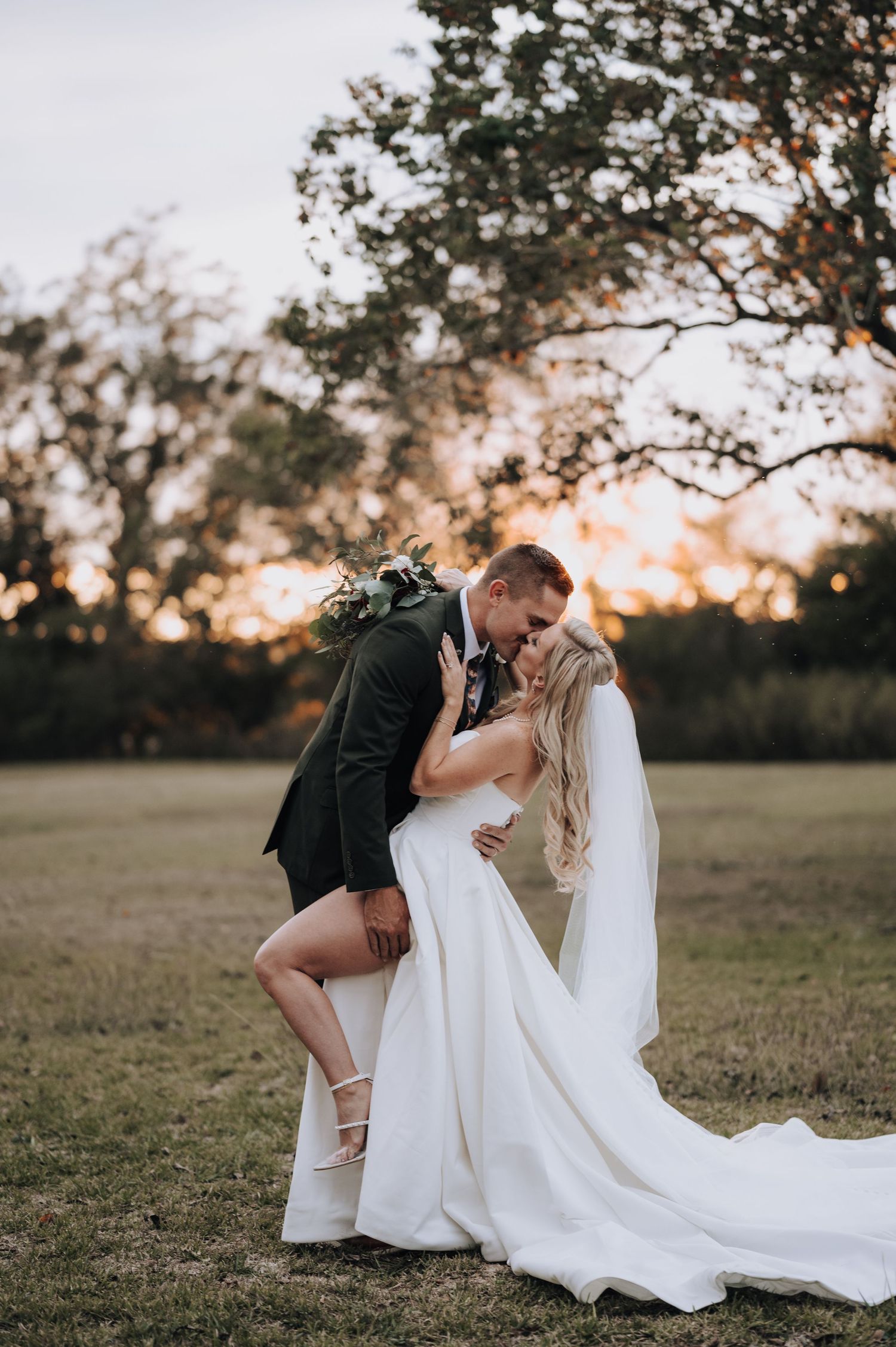 Dramatic sunset wedding photo showing couple embracing in open field with flowing white dress.