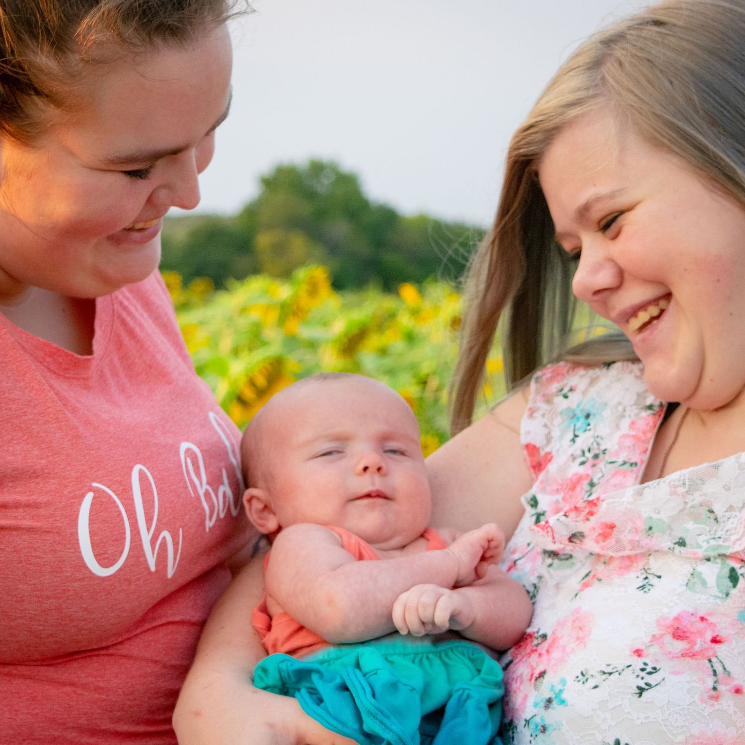 LGBTQIA Newborn and Maternity Session. Moms hold baby and smile at her. Missouri Sunflower Patch