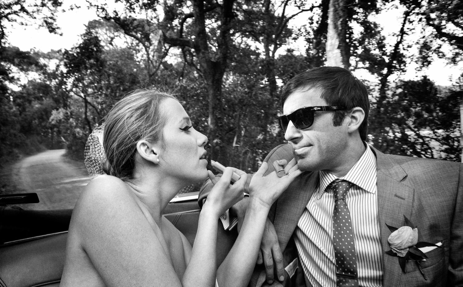The bride fixes her lipstick using the reflection of her husband's sunglasses.