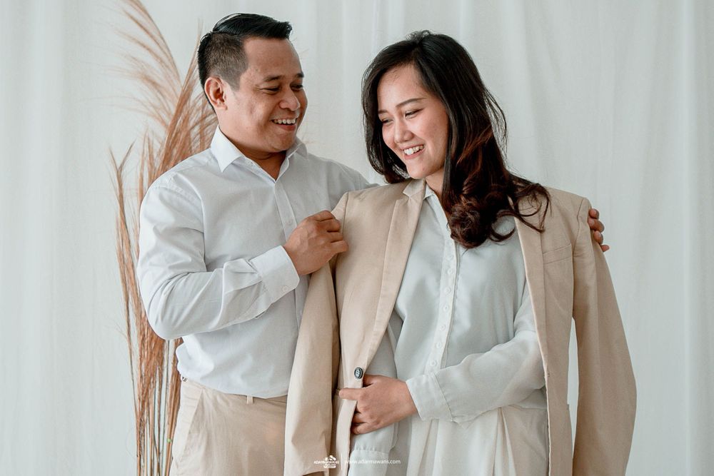 A couple in matching light-colored outfits shares a candid moment against a white backdrop.