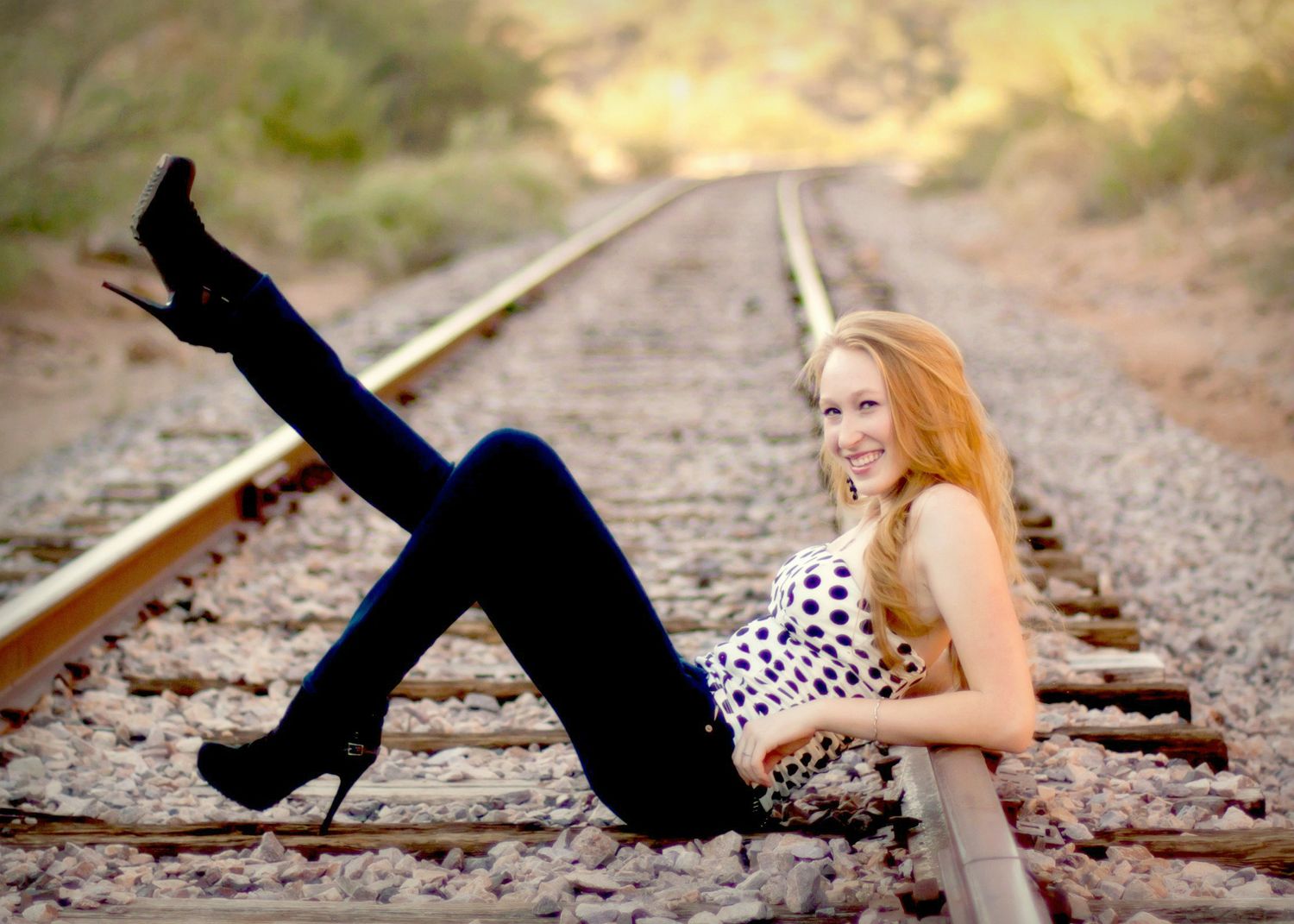 Portrait of a senior girl reclined on train tracks, with one leg kicked up in the air.