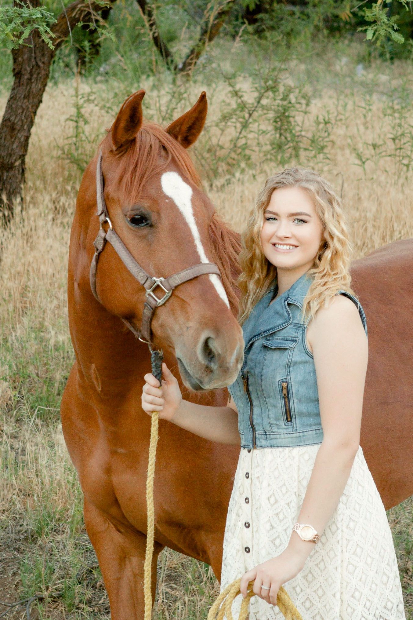 Portrait of a senior girl standing next to her horse, with its bridal in her hand.