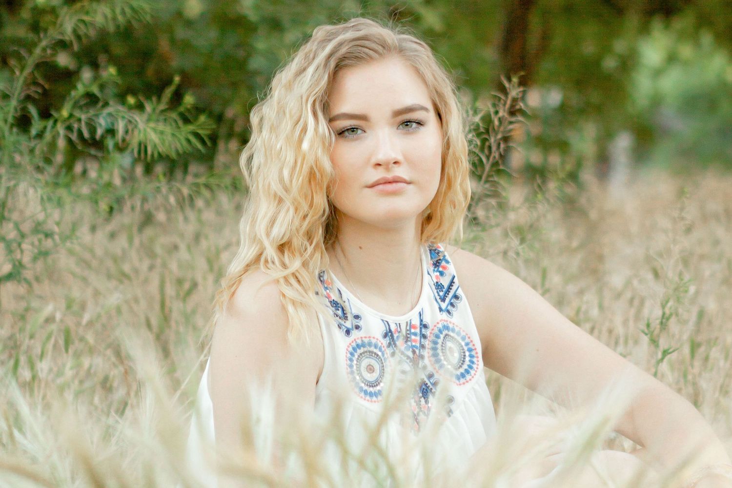 Portrait of a senior girl sitting with her arm propped on her knee in a grassy field
