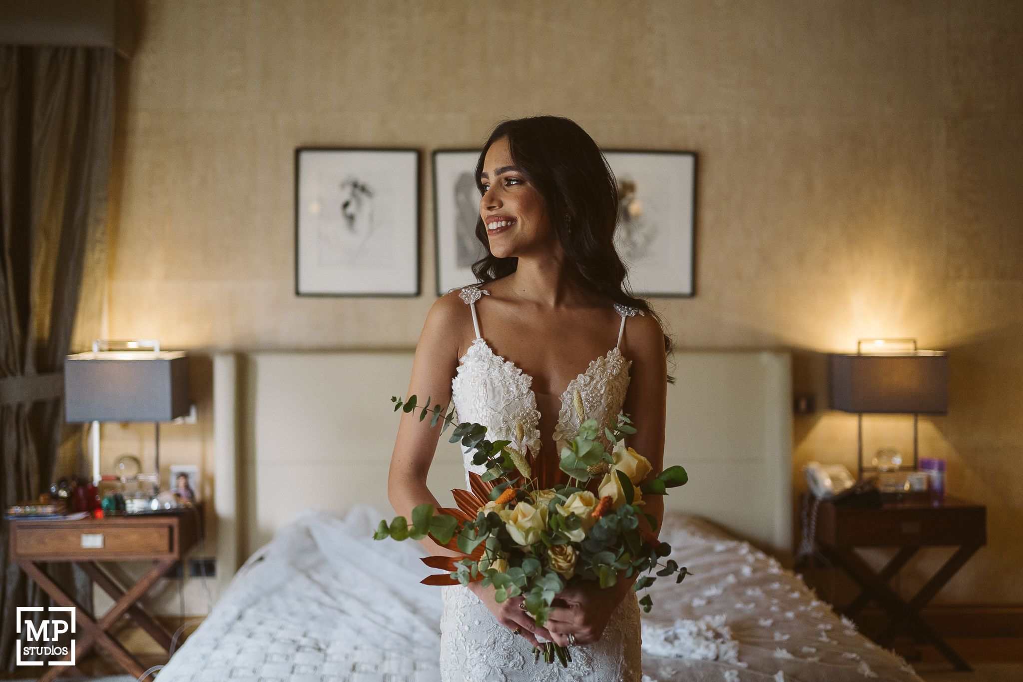 Someone in a white dress holding a beautiful bouquet of flowers in a warmly lit bedroom.