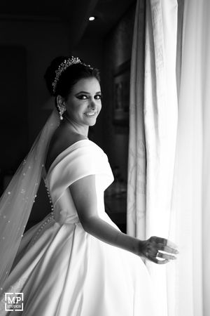 Classic black and white bridal portrait by window showcasing elegant wedding dress and veil.