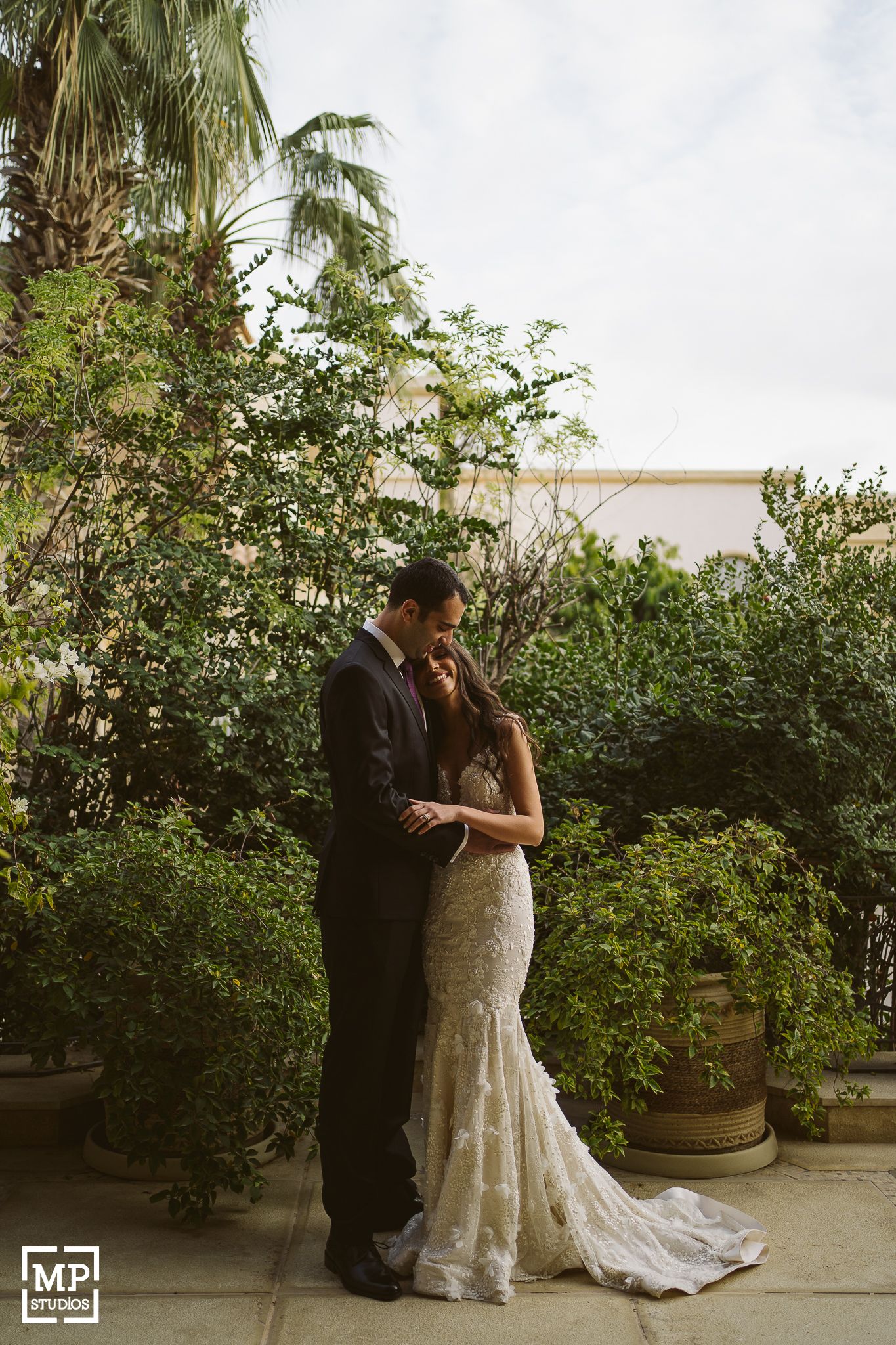 A romantic wedding portrait of a couple standing by tropical foliage and palm trees.