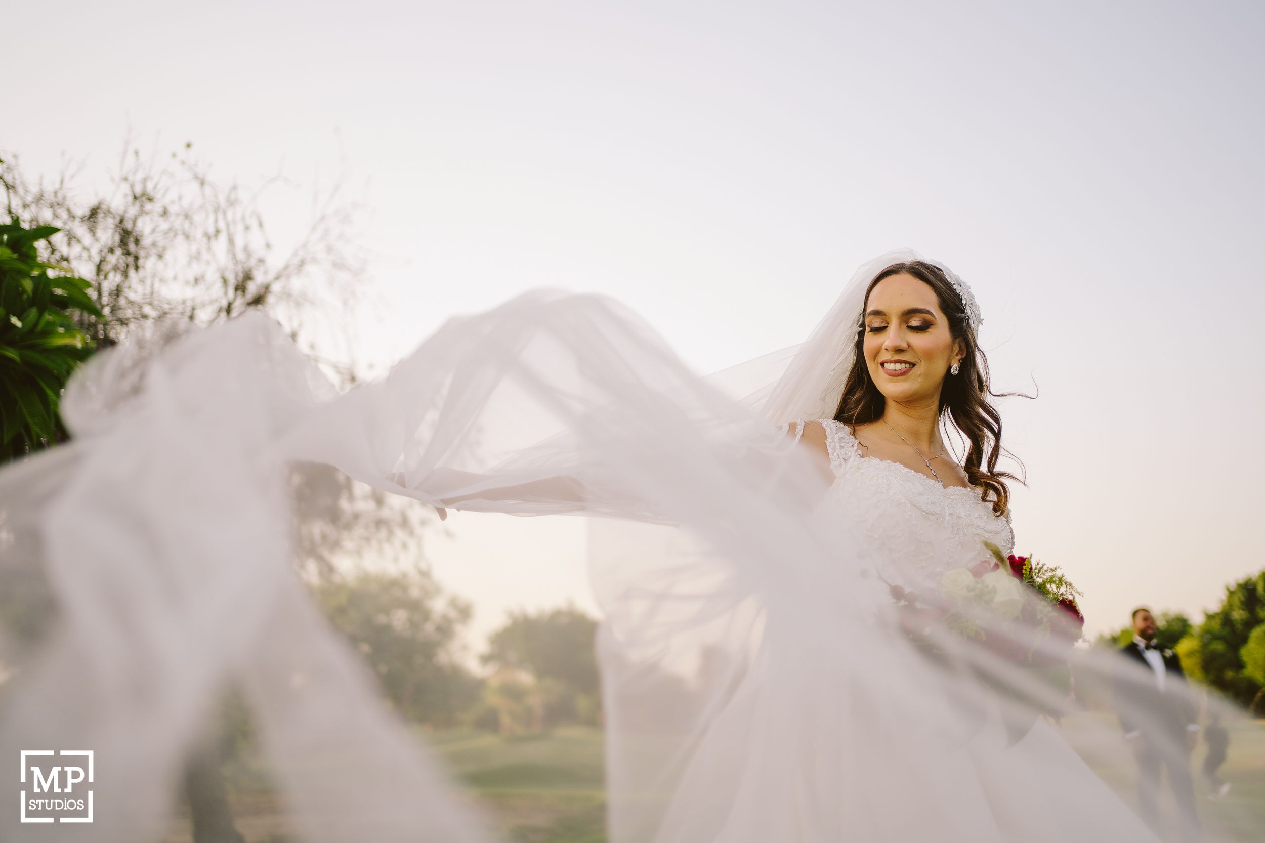 A bride in a flowing white wedding dress twirls outdoors creating a dramatic effect with the veil.