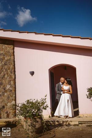 A couple shares an intimate moment in the doorway of a pink Mediterranean-style building.