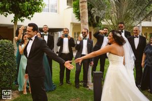 Wedding party celebrates outdoors as newlyweds share a playful moment in their formal attire.