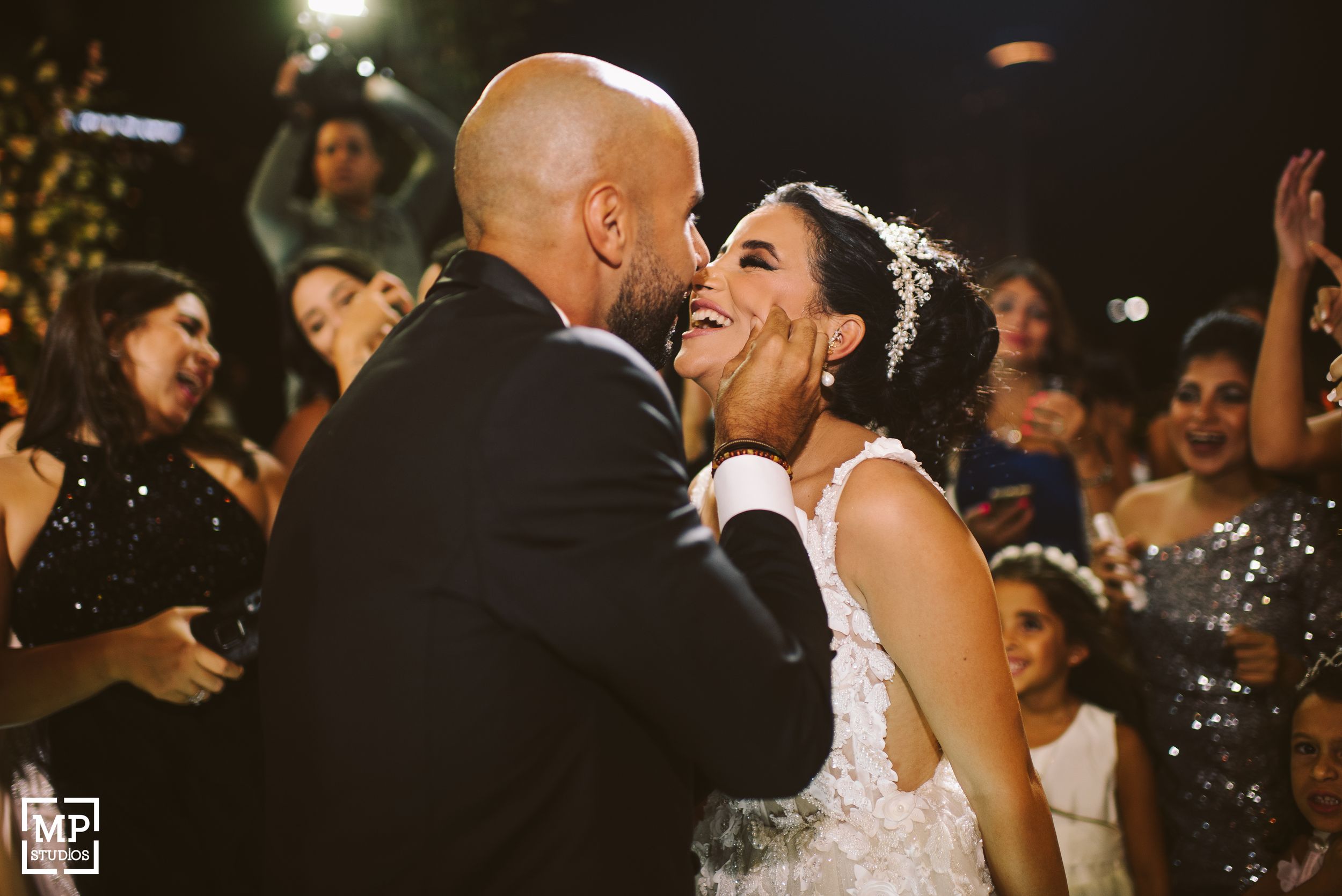A couple shares an emotional moment during their wedding reception with guests cheering in the background.