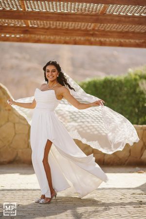 Bride in flowing white dress twirls gracefully under rustic pergola in desert setting.