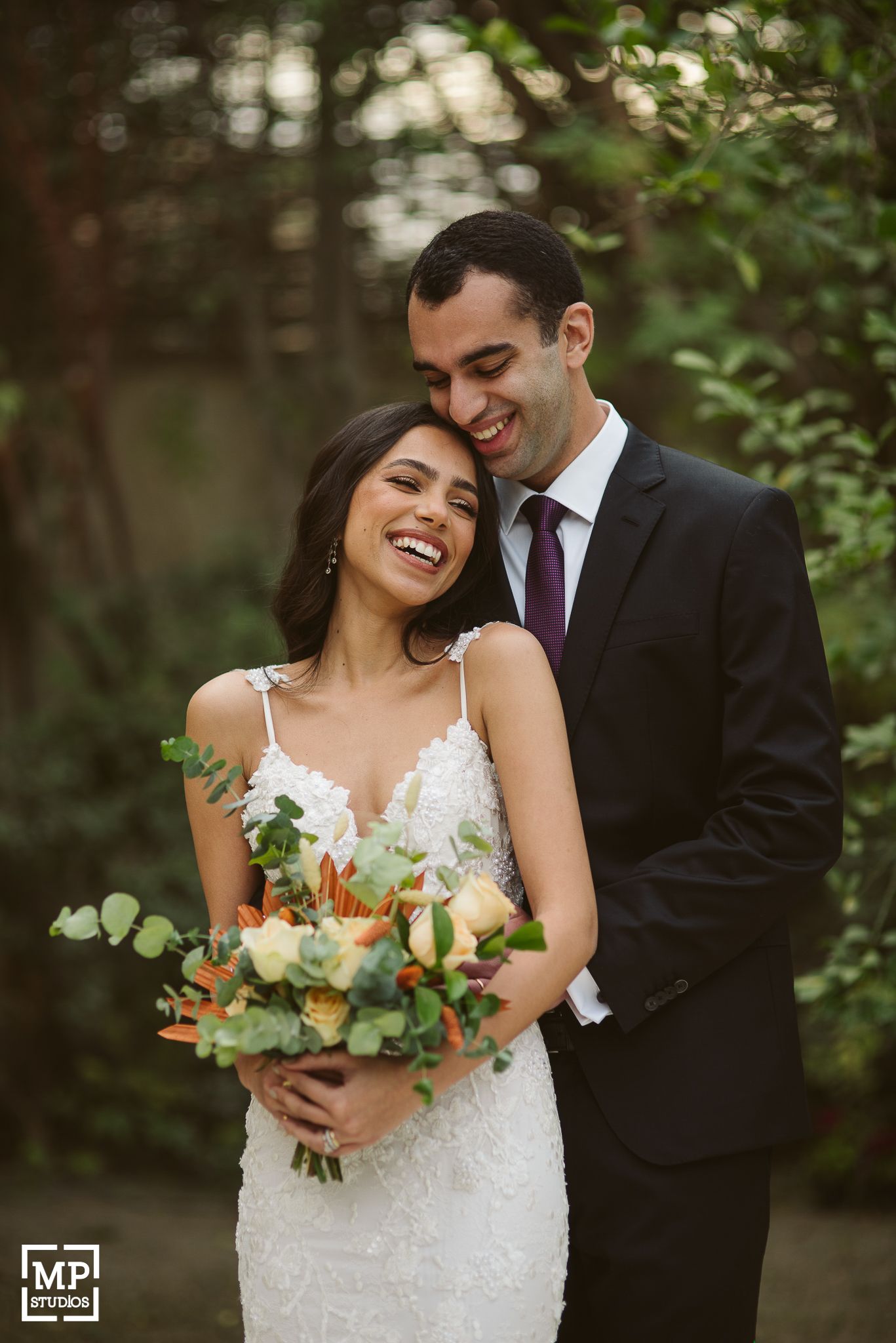 Joyful newlyweds share an intimate moment in a garden setting with the bride holding a colorful bouquet.