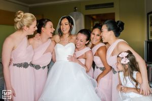 Bridal party in pink bridesmaid dresses share a joyful moment with bride in white gown during wedding preparations.