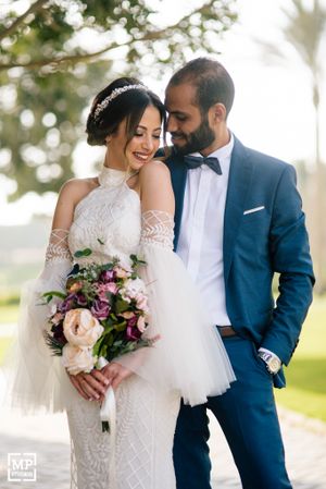 Newlyweds share an intimate moment outdoors as bride holds a beautiful bouquet of mixed flowers.