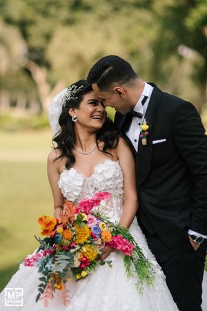 Joyful wedding moment captured outdoors with vibrant colorful bouquet against natural background.