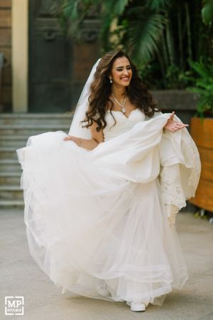 Bride in flowing white dress twirls joyfully in garden setting.