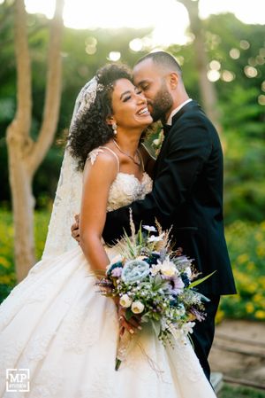 Romantic wedding portrait with beautiful bouquet featuring blue and purple flowers against garden backdrop.