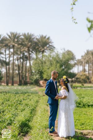 Wedding couple standing in lush green field with palm trees in background.