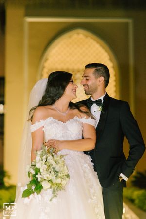 Romantic nighttime portrait of newlyweds sharing an intimate moment under ornate archway.
