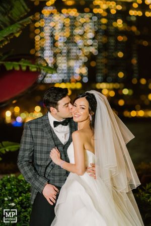 Romantic couple embrace under twinkling lights at nighttime wedding celebration.