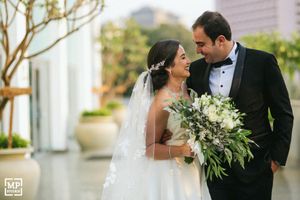 Elegant wedding couple shares intimate moment with white floral bouquet in outdoor setting.