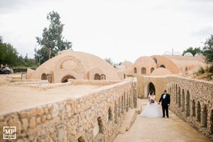 Couple walks along stone archway path at desert wedding venue with domed architecture.