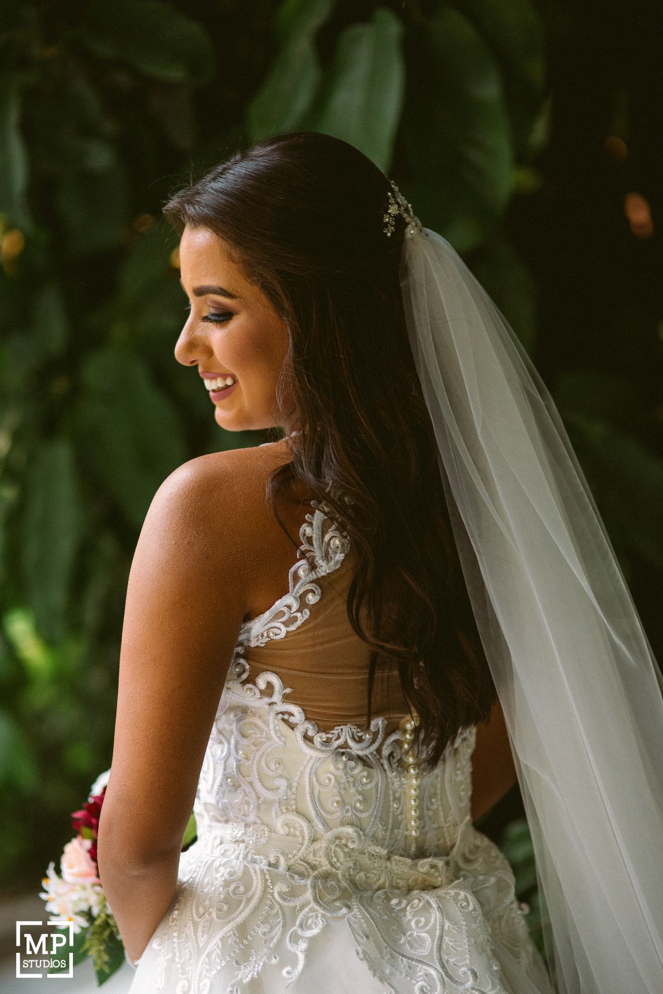 Back view of bride showing intricate lace detail of wedding dress against green foliage.