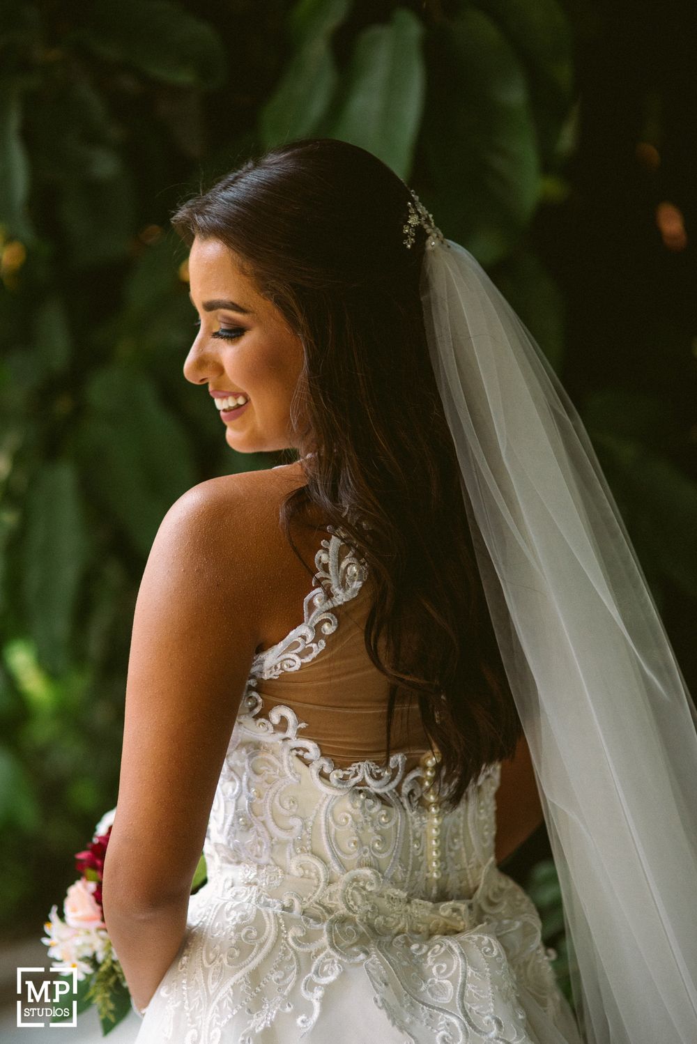 Back view of bride showing intricate lace detail of wedding dress against green foliage.