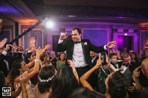 Wedding reception dance party with energetic celebration on crowded dance floor with purple lighting.