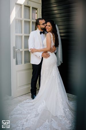 Elegant couple in formal wedding attire poses against white door and dark wall for romantic portrait.