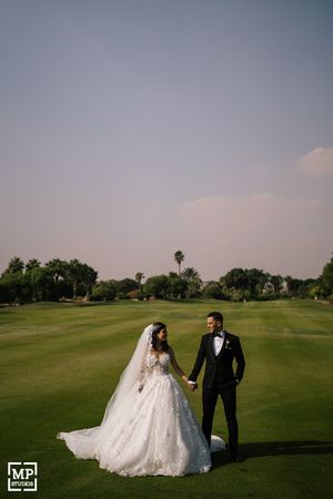 Newlywed couple poses on golf course with dramatic sky and palm trees in background.