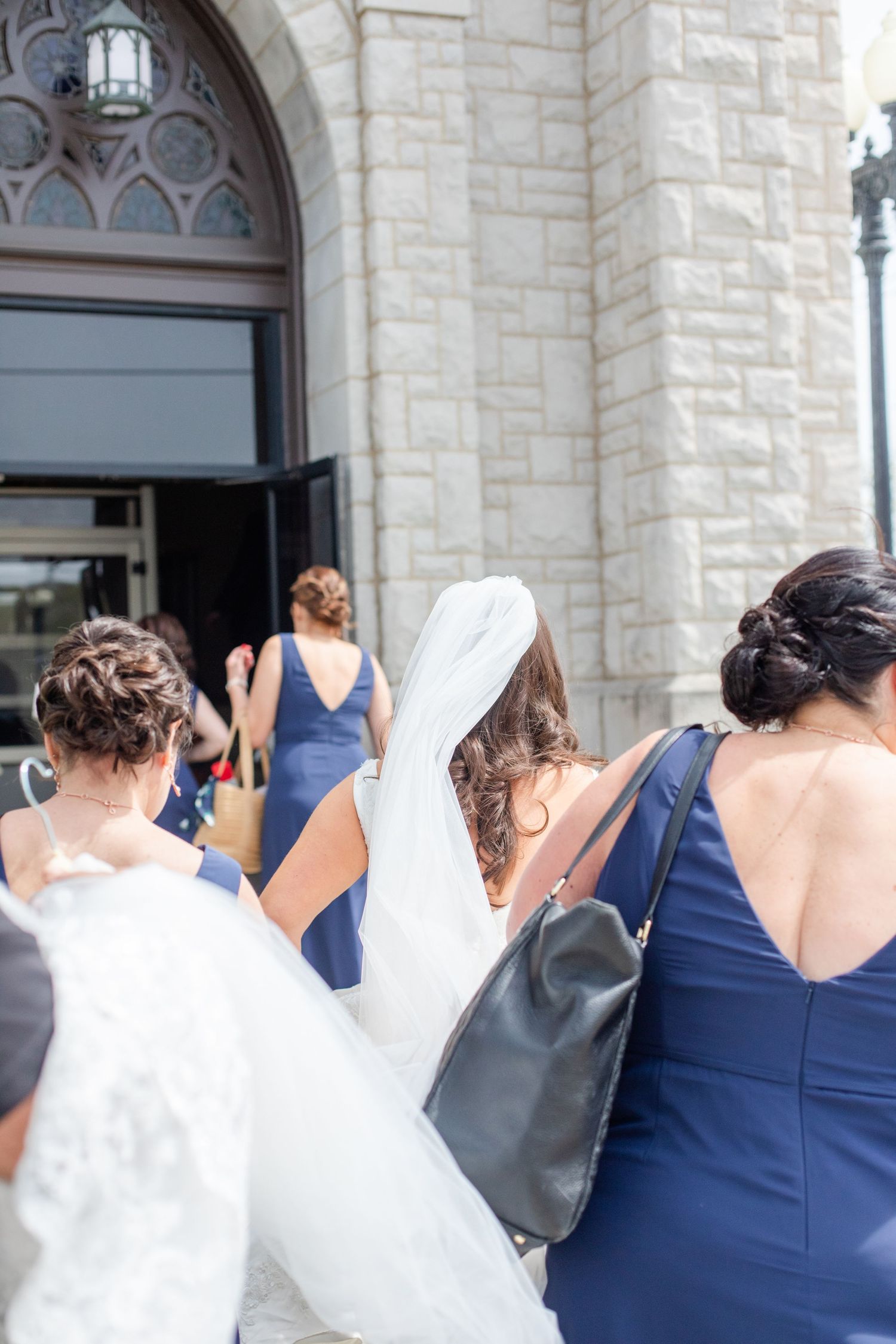 Wedding party in navy blue and white attire gathered outside stone church building.