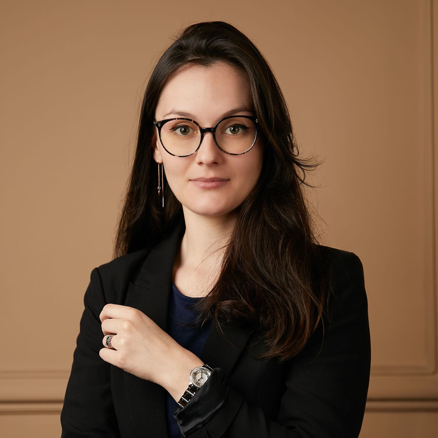 Professional portrait of a person in business attire wearing glasses against a brown background.