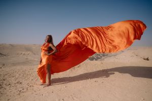 Vibrant coral fabric catches wind creating beautiful movement in sandy desert landscape.