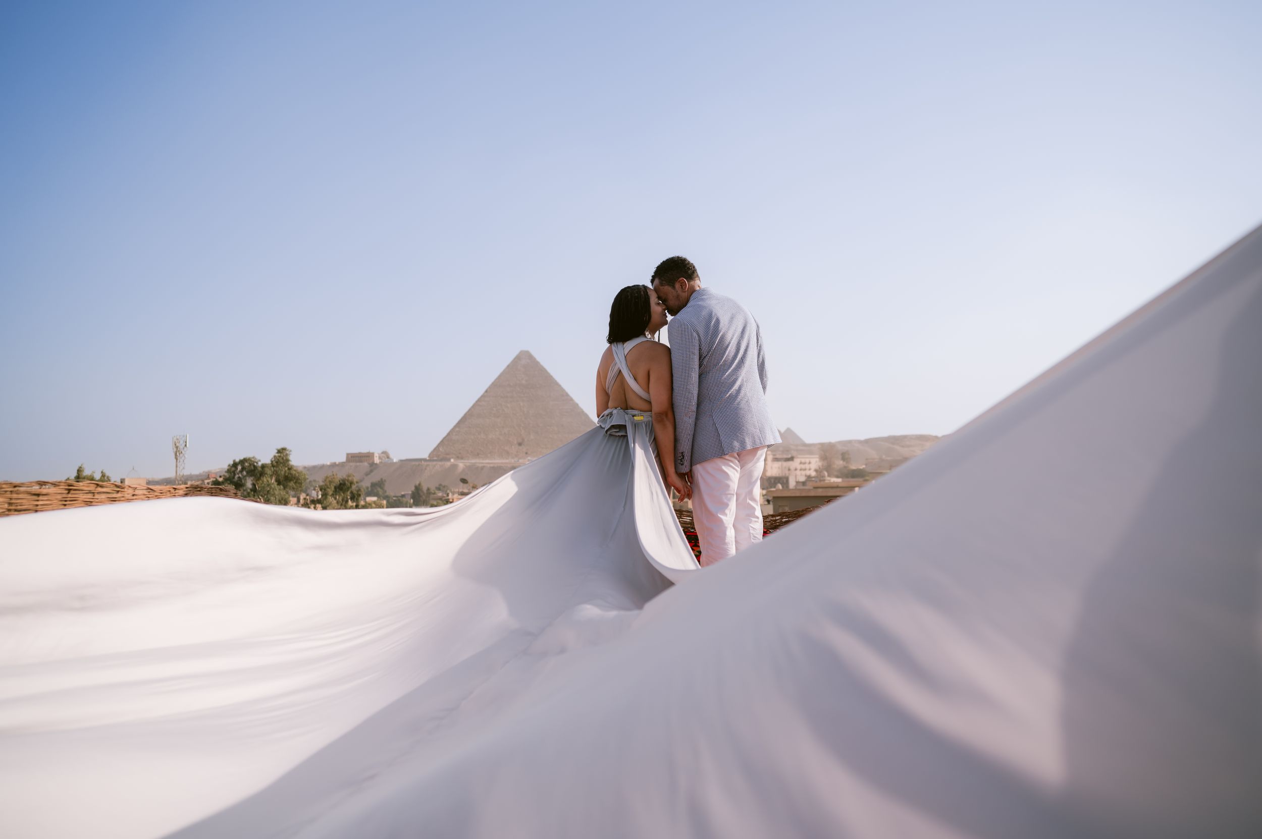 White flowing fabric creates dreamy frame against Egyptian pyramid landscape.