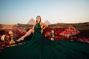 Emerald green dress flows dramatically against Egyptian pyramid backdrop with traditional carpets at sunset.
