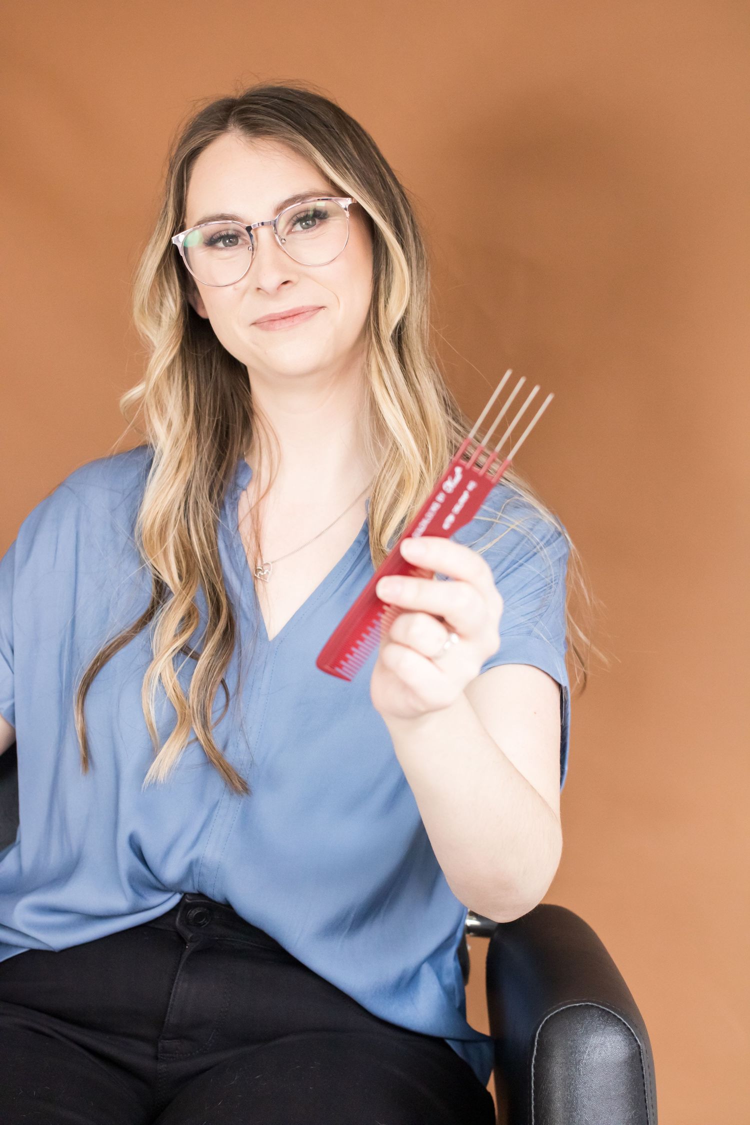 Hairstylist in blue shirt holding styling comb against orange backdrop.